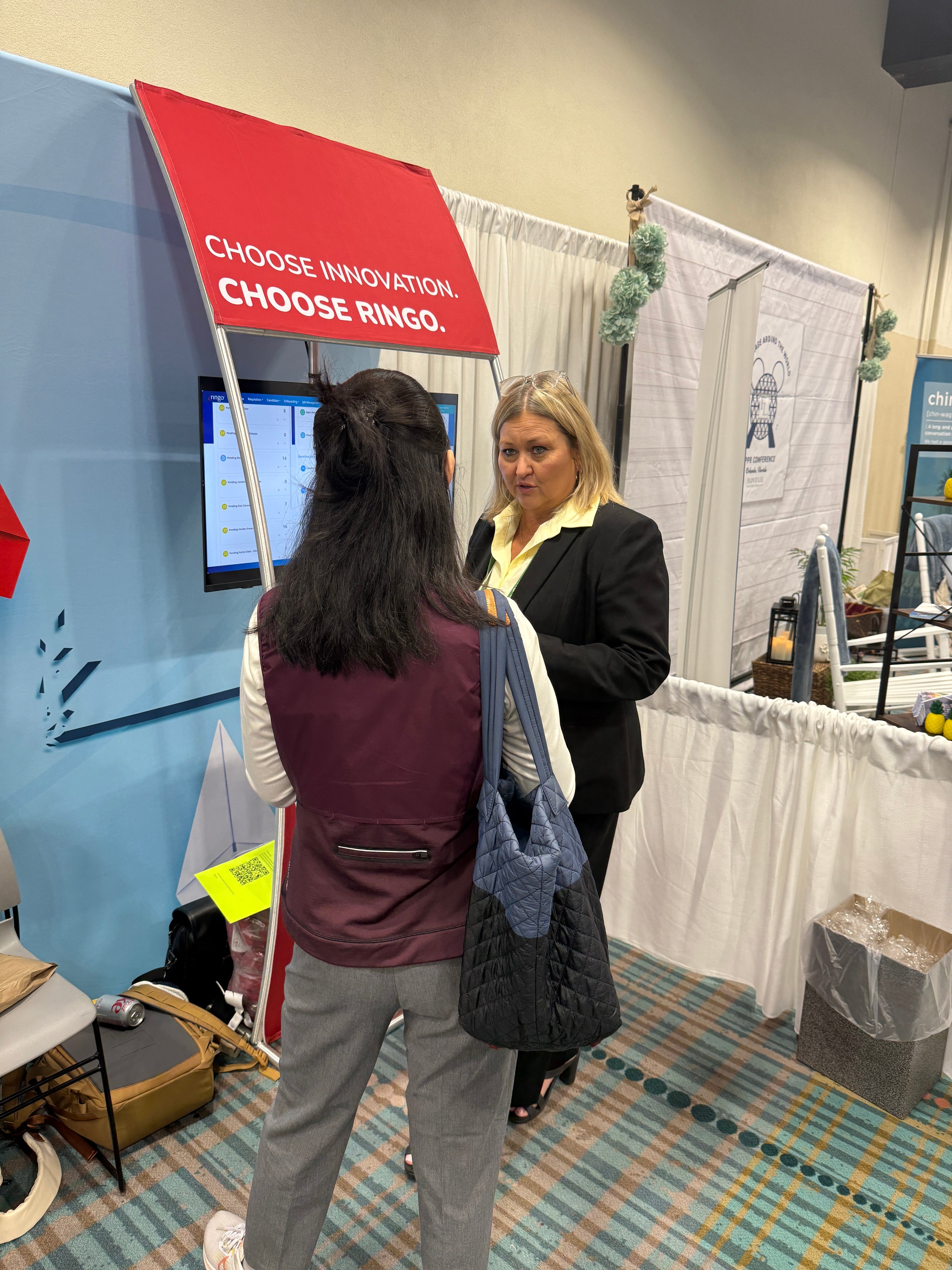 Healthcare leader discussing workforce management technology at Ringo booth during AAPPR conference, reviewing platform capabilities on screen.