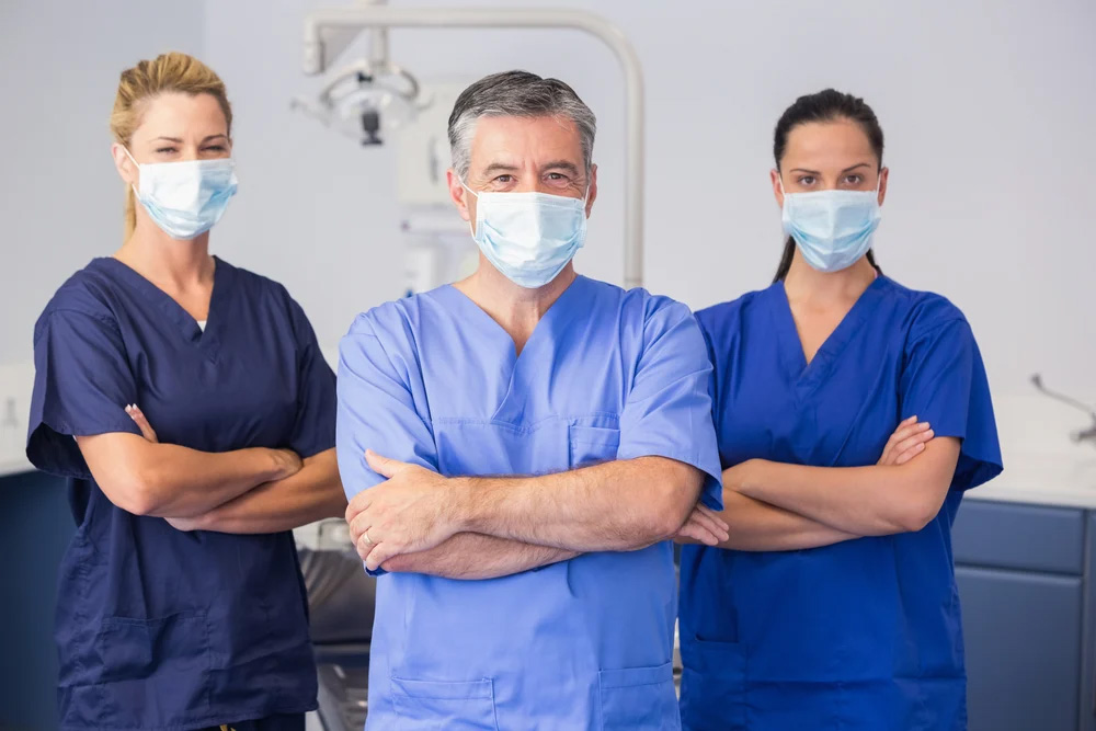 Three healthcare professionals standing with their arms crossed wearing masks