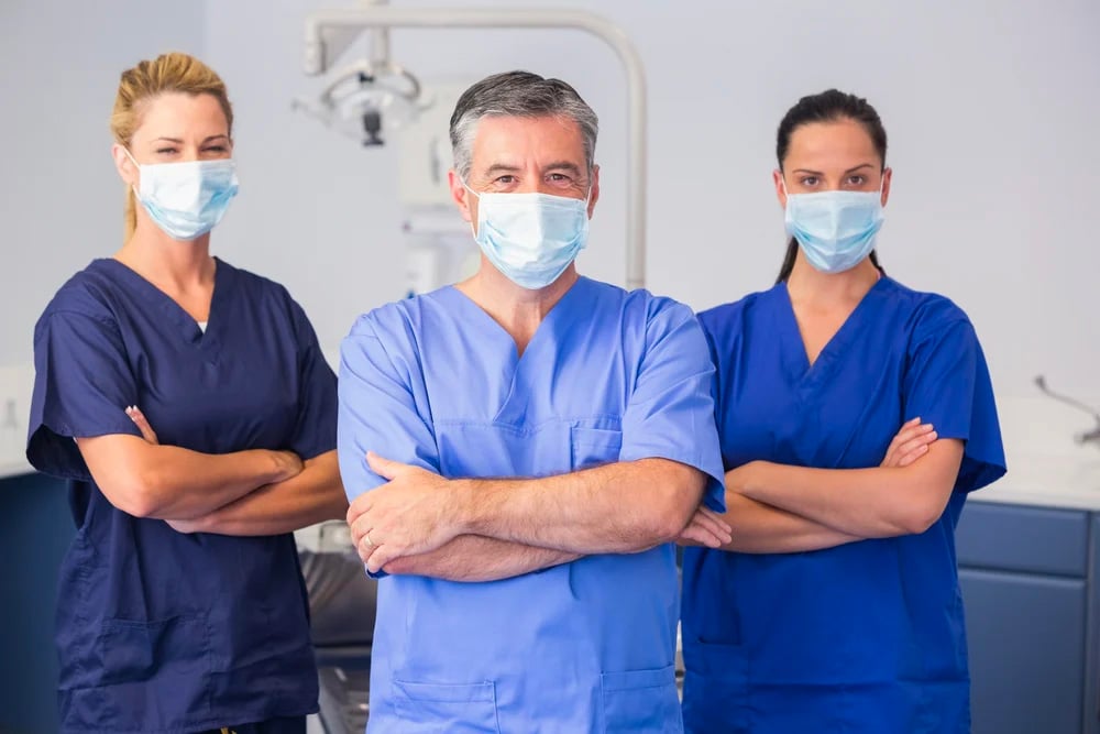 Three healthcare professionals standing with their arms crossed wearing masks